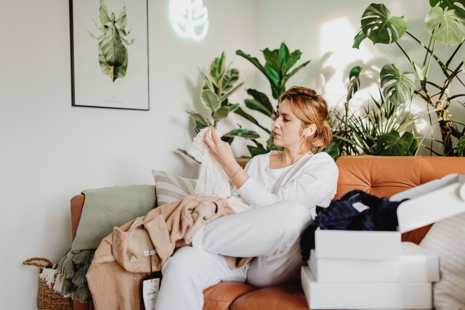 Woman examining clothes on a cozy sofa with many houseplants around.