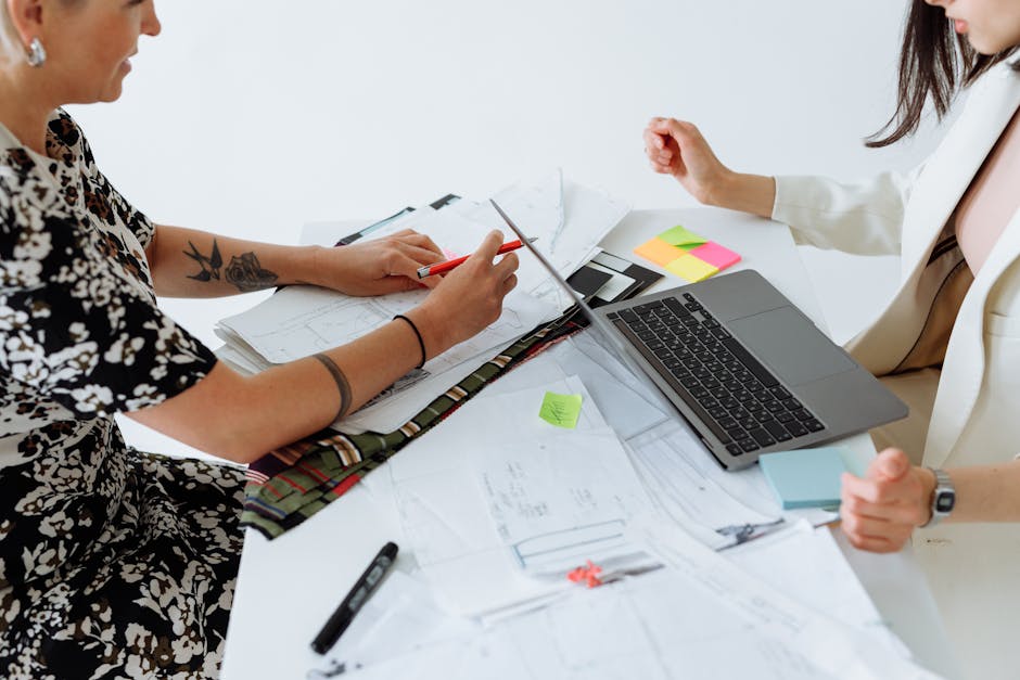 Two women collaborating on a project with documents and laptop, highlighting teamwork.