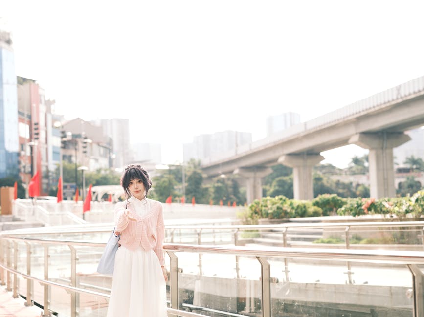 Casual portrait of a stylish woman standing near a railing in a modern cityscape setting.