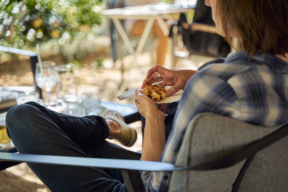 Person in plaid shirt enjoying food outdoors, seated comfortably with blurred background.