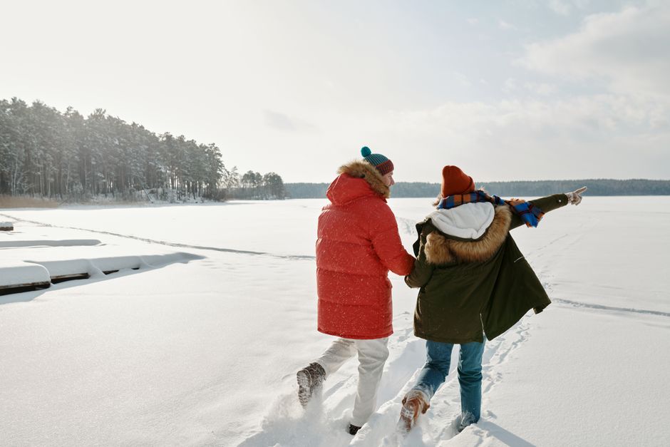 A couple walking on a snow-covered field wearing winter clothing, pointing at the distance.