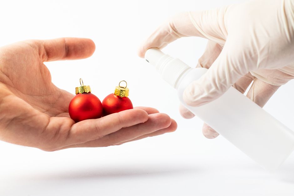 Close-up of hands spraying disinfectant on red Christmas baubles for holiday hygiene.